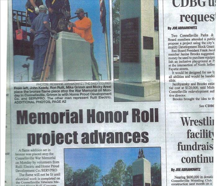 A Newspaper Clipping of a SERVPRO employee placing bronze flame piece on top of a memorial.
