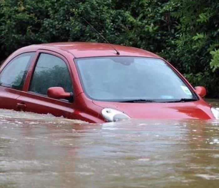 A picture of a red car driving through flood waters.
