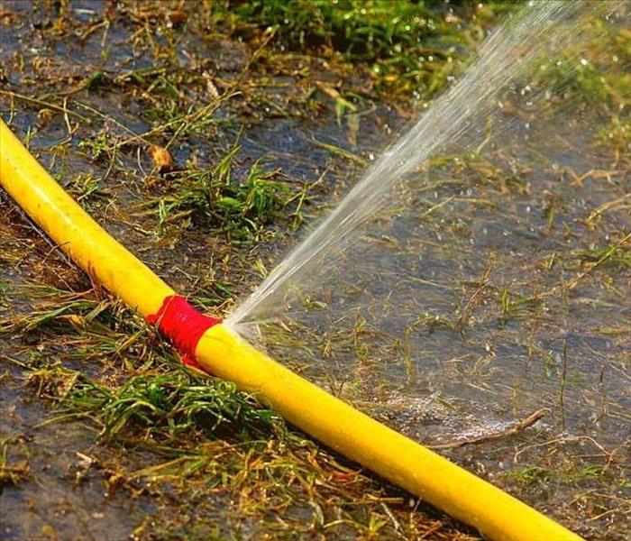 A picture of a yellow hose leaking water while flooding the yard.